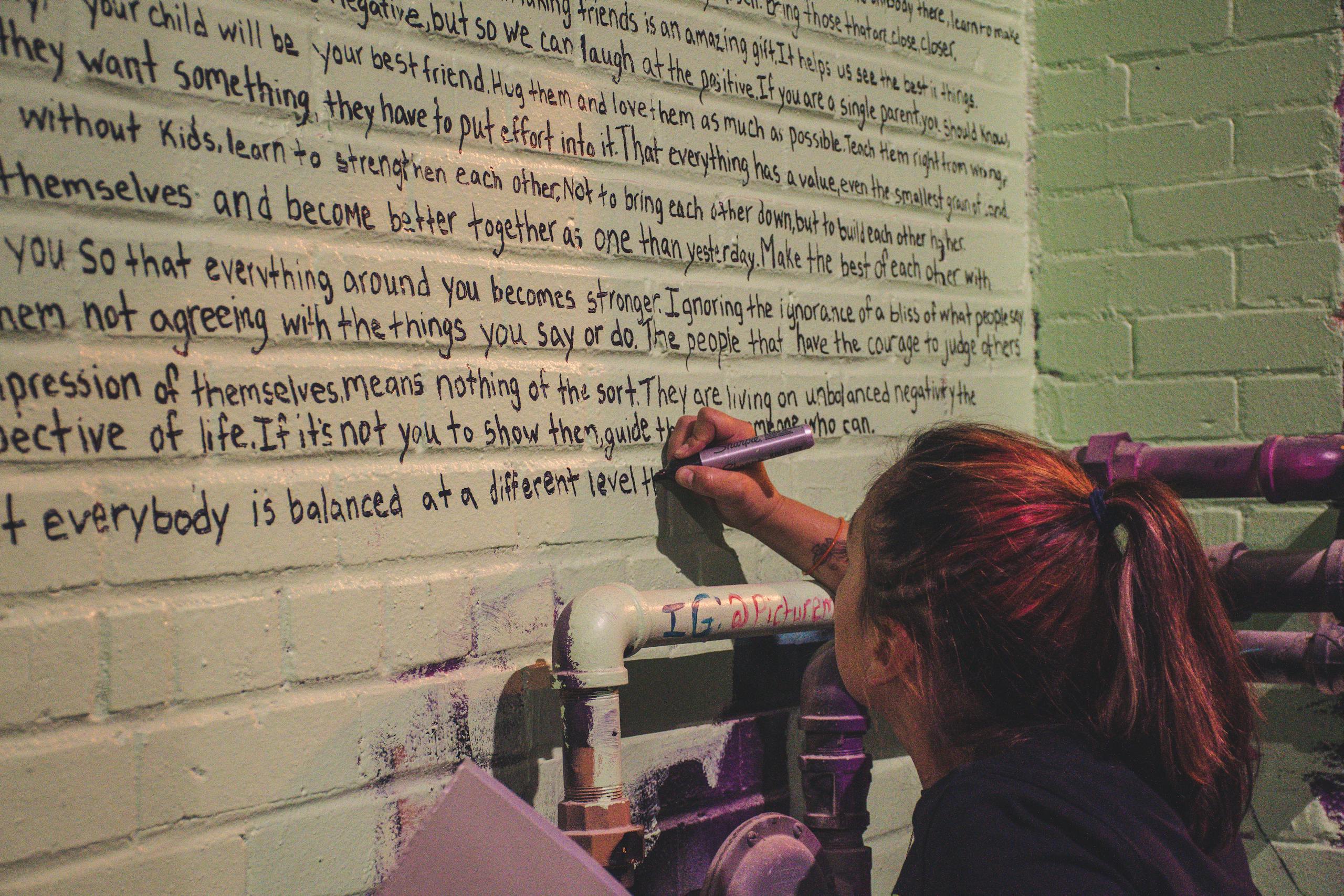 A woman writing motivational phrases on a brick wall in an industrial setting.